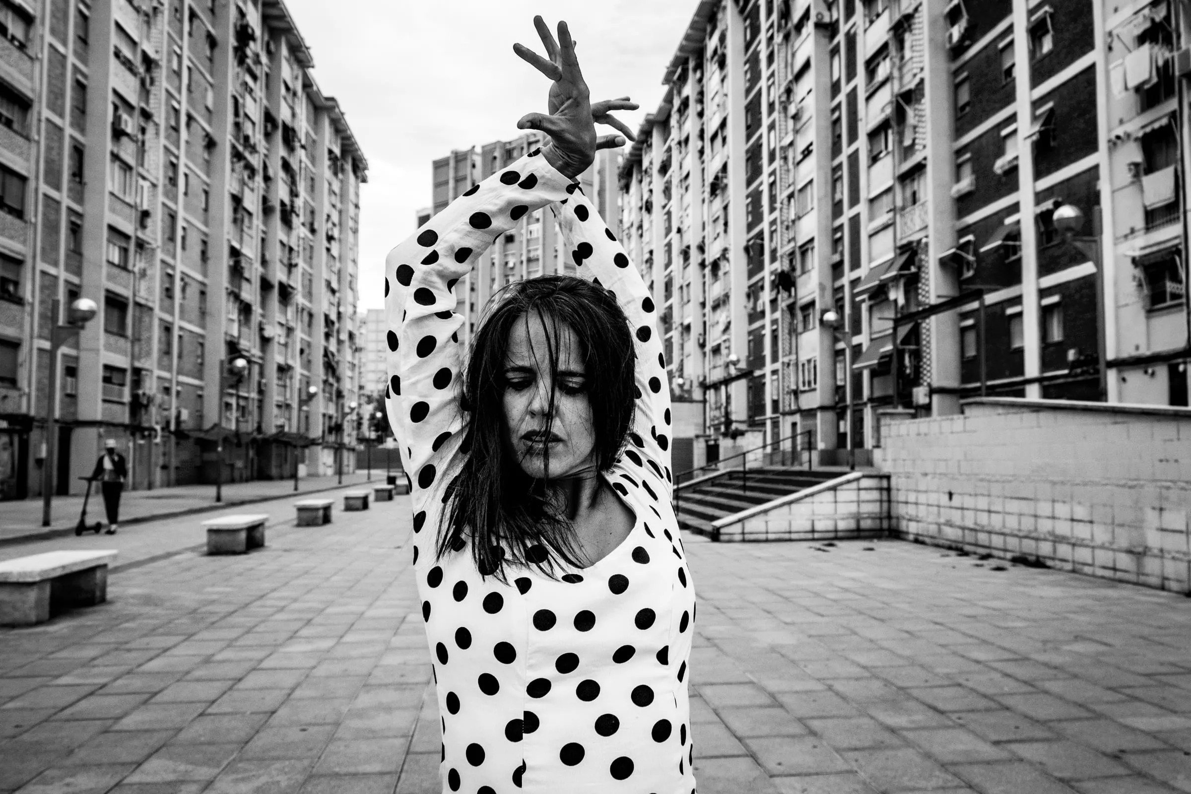 Aina Núñez, con mantón de lunares, baila en medio de una calle entre bloques de viviendas.