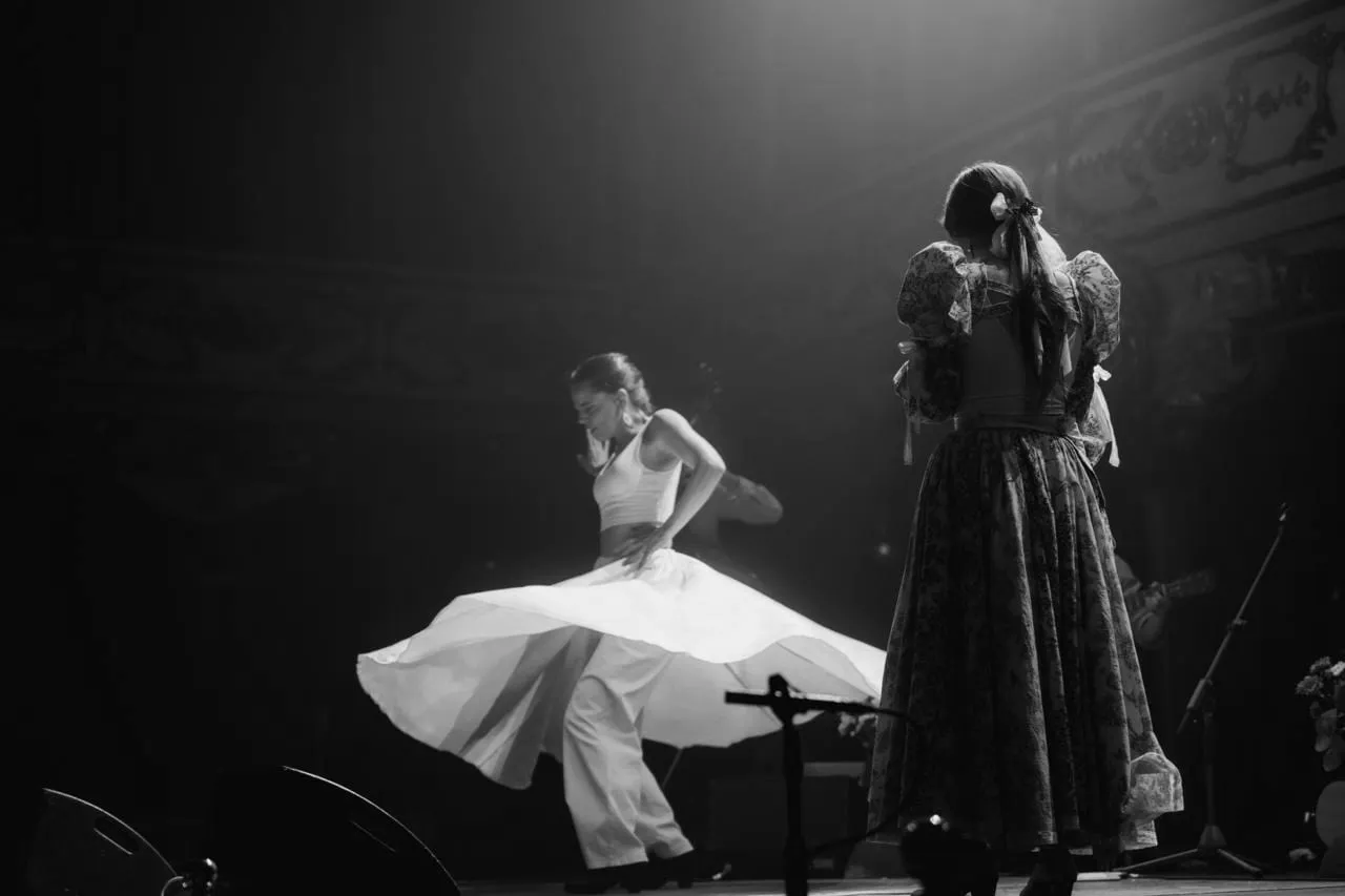 Aina Núñez gira con la falda abierta en un teatro, junto a una cantante de espaldas.