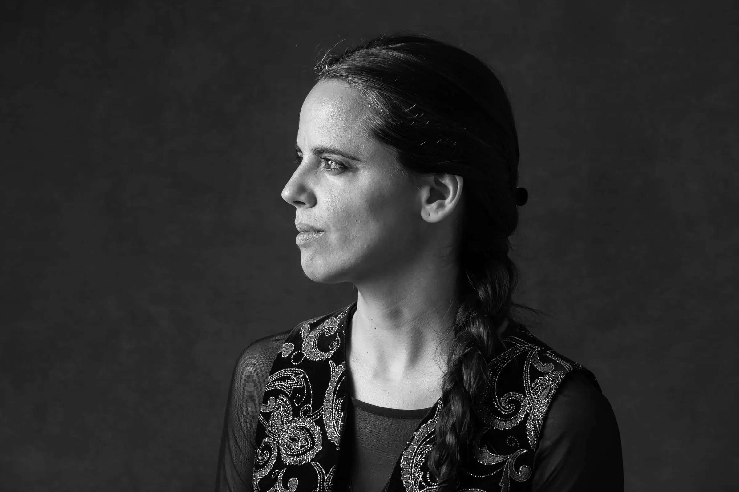 Retrato de Aina Núñez de perfil, sentada sobre fondo oscuro, con un chaleco bordado.